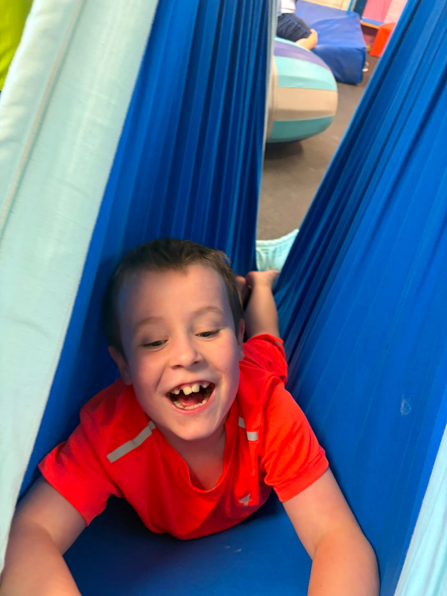 A laughing boy peeking out of a blue sensory swing at the ASD Ireland summer camp.