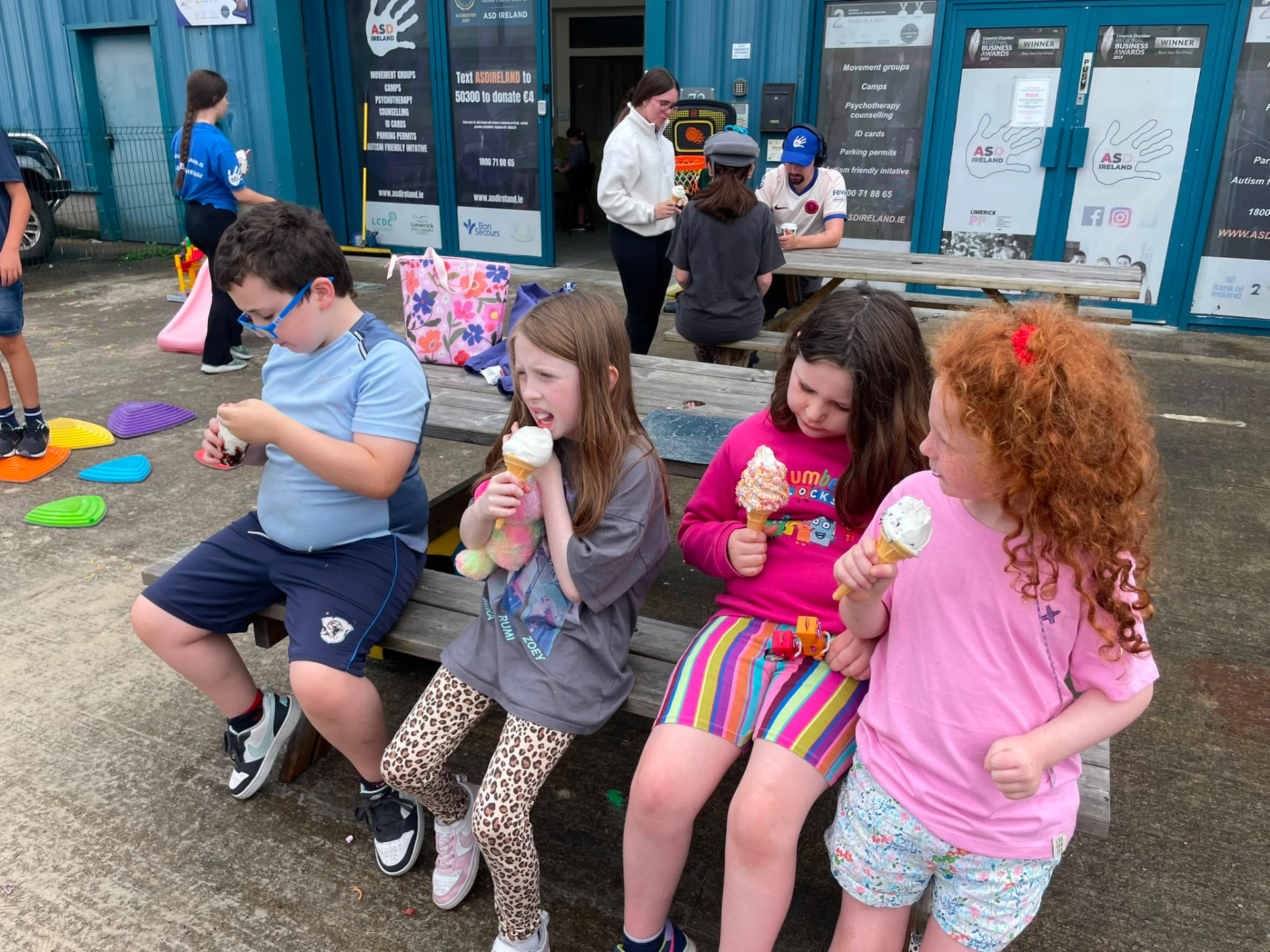 Children enjoying ice cream together on a bench outside the ASD Ireland centre during summer camp.