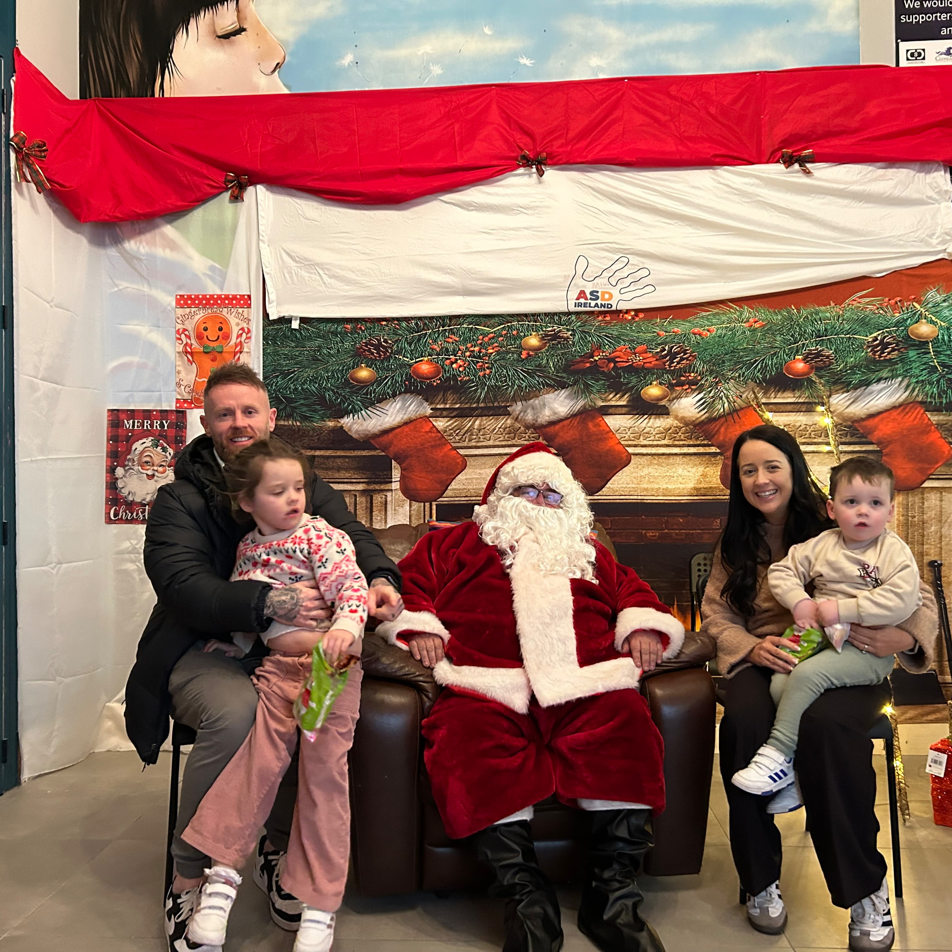 A family sitting with Santa in front of the ASD Ireland Christmas banner.