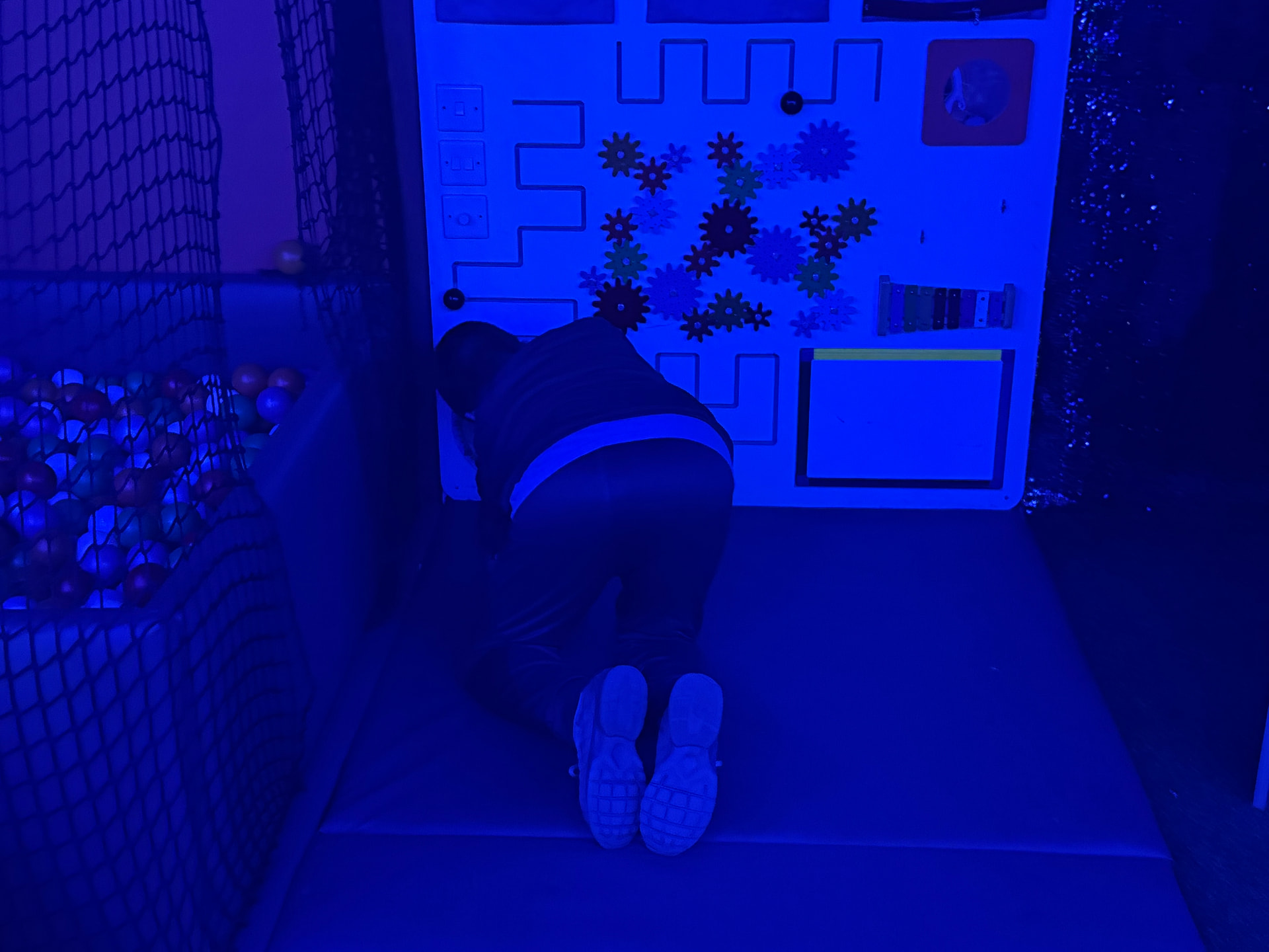 Inside the mobile sensory room: a child exploring a tactile activity wall of gears, switches and mazes beside the ball pit.